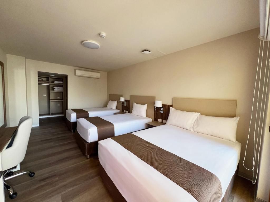 Een hotelkamer met drie bedden, een bureau en een stoel.