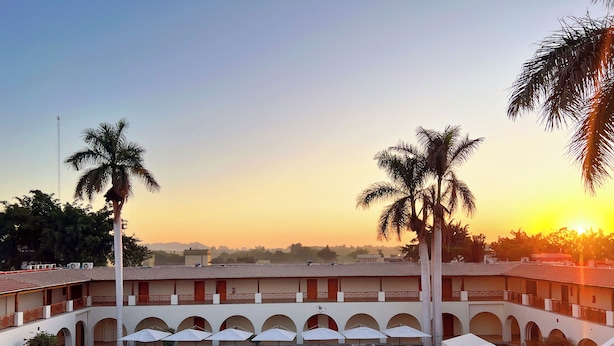Pátio de hotel com piscina, espreguiçadeiras e palmeiras.