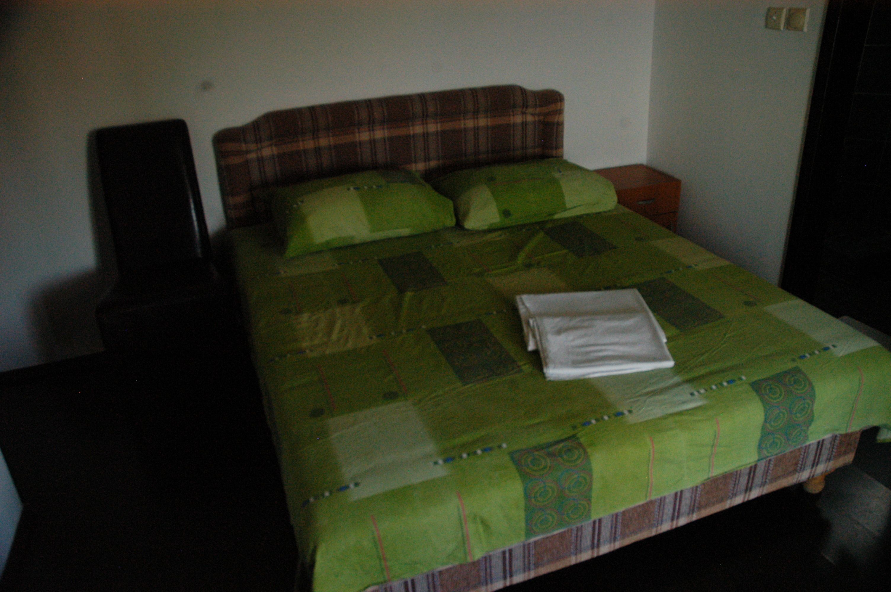 Una cama con un edredón verde, una almohada y una toalla doblada.