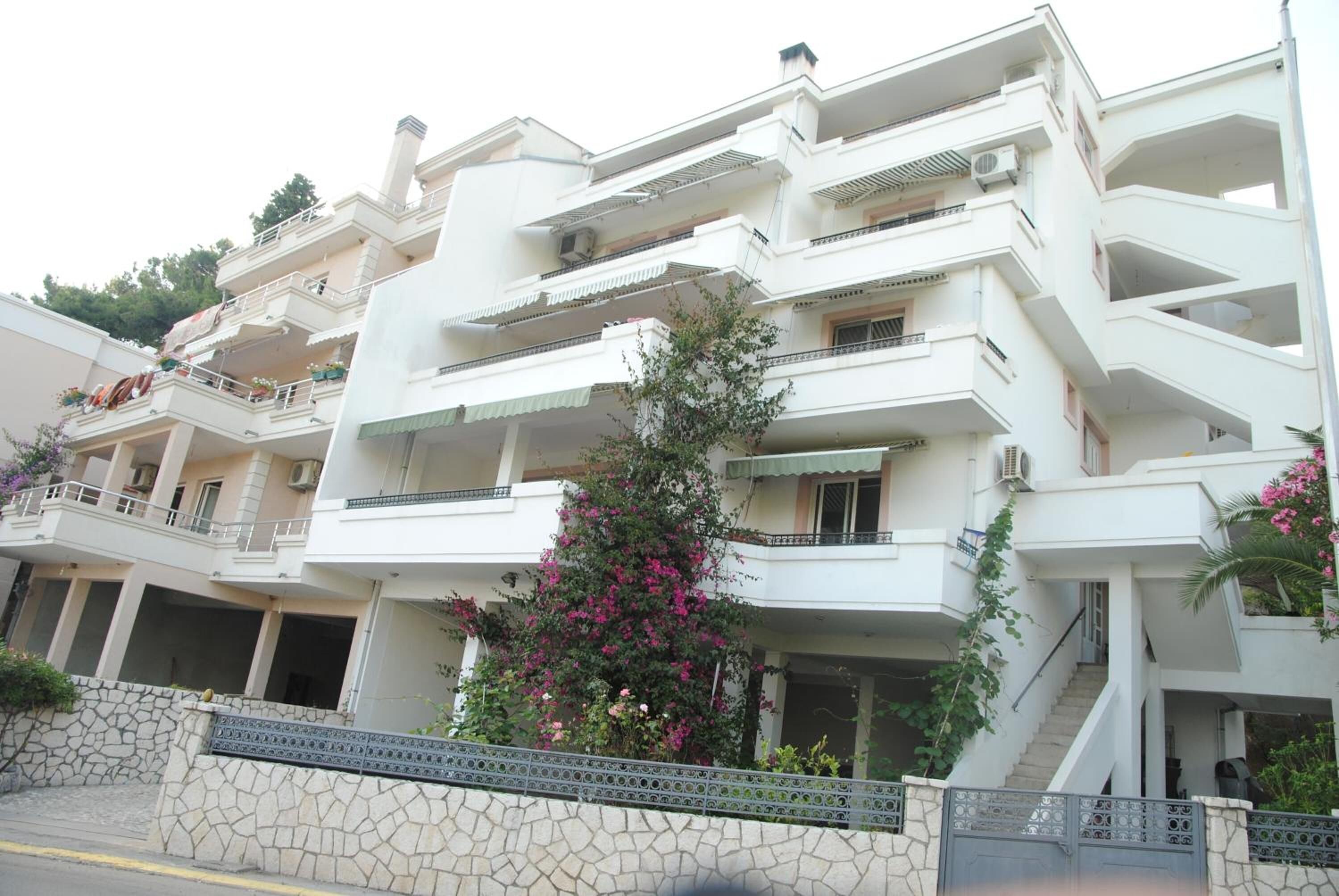 A multi-story residential building with balconies, a stone wall, and a staircase leading to the upper floors.