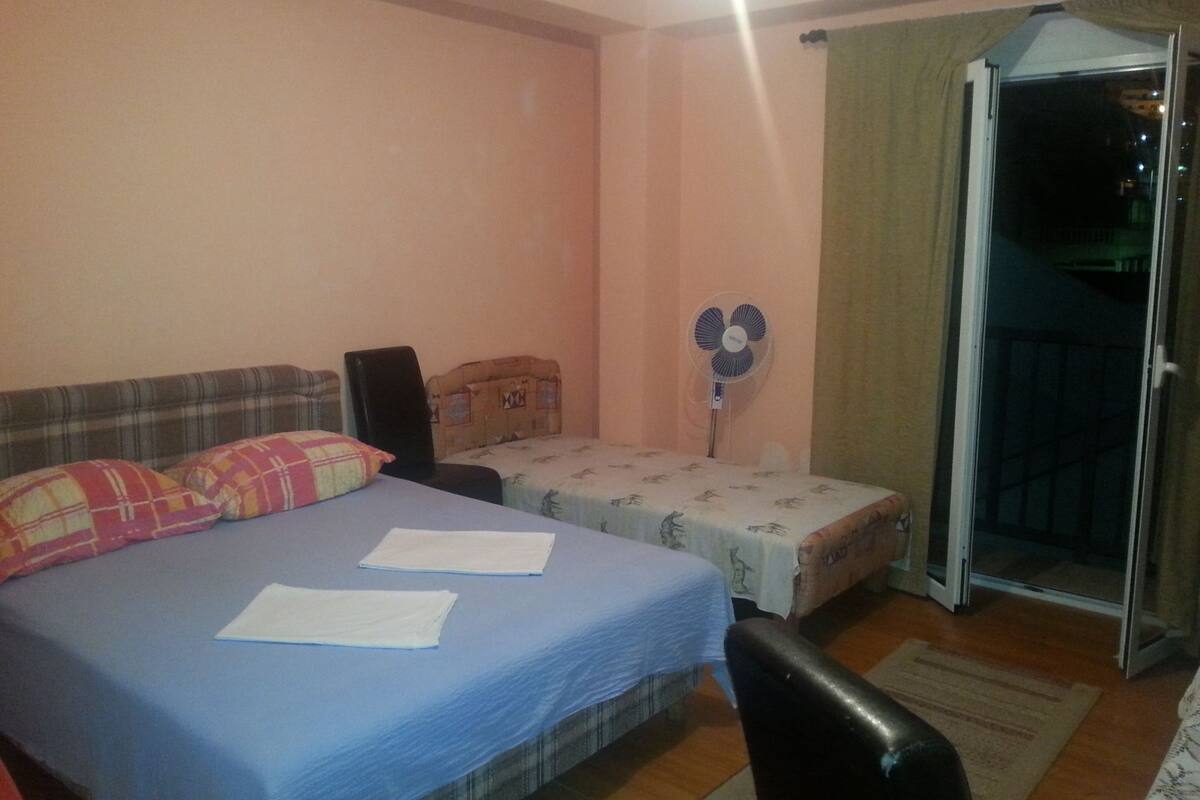 Un dormitorio con dos camas, un ventilador, una silla y un puertas corredera que da a un balcón.