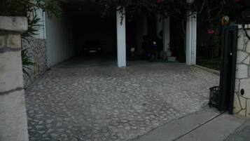 Een verharde oprit die leidt naar een garage, met aan één kant een stenen muur en aan de andere een zwart hek.