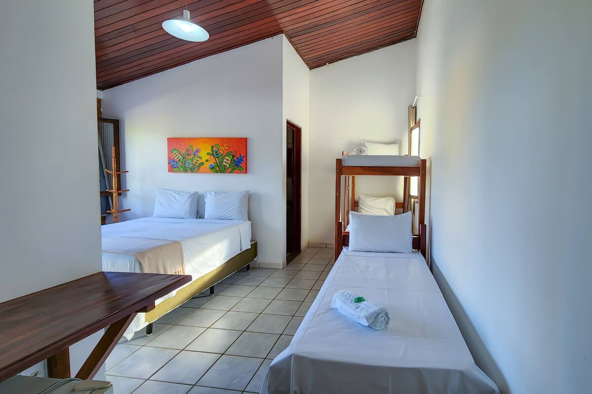 A hotel room with two beds, a wooden bench, a painting, and a tiled floor.