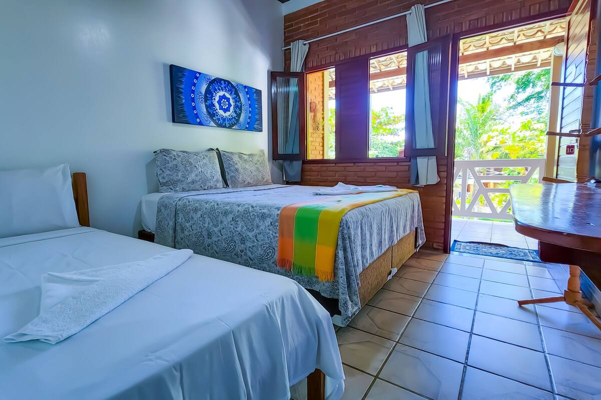 A hotel room with two beds, a balcony, and a view of greenery.