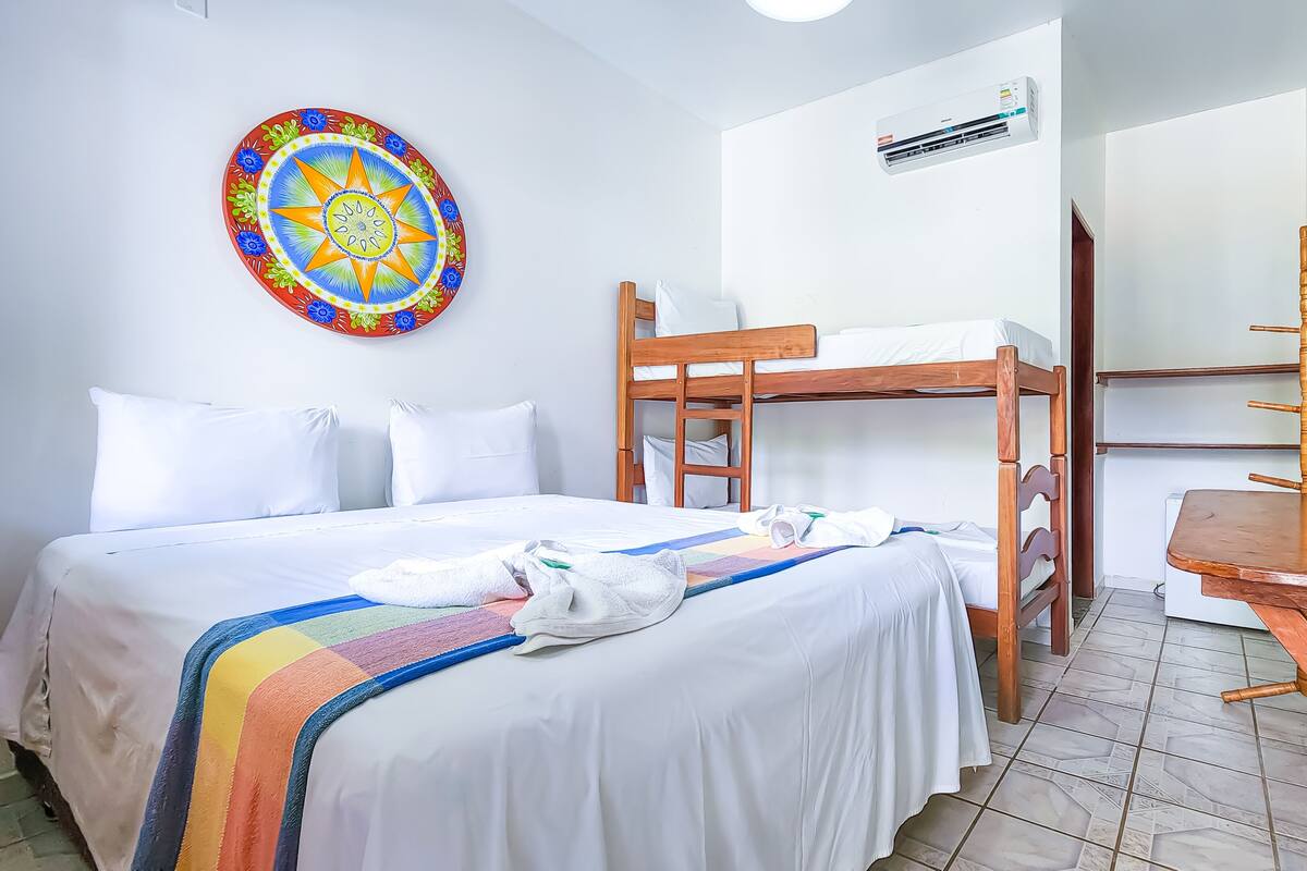 A hotel room with a bunk bed, a desk, a colorful wall decoration, and a TV mounted on the wall.