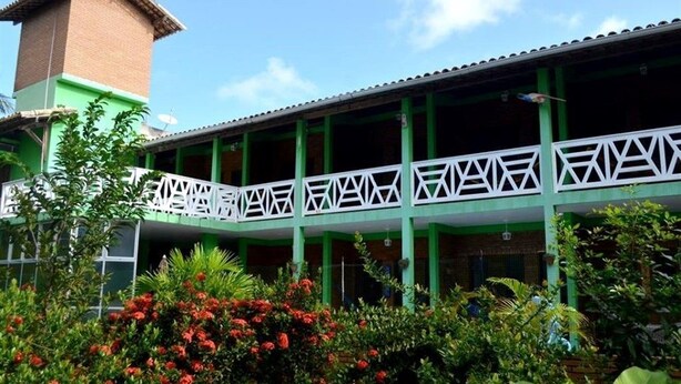 A building with a green facade, a white balcony railing, and a brick chimney. - Pousada Encantos da Natureza (Marechal Deodoro)