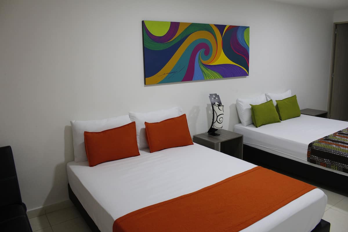 A hotel room with two beds, each with white linens and orange accents. There is a colorful abstract painting on the wall above the beds.