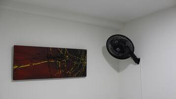Una habitación con cama, un ventilador de pared y un cuadro abstracto de gran tamaño.