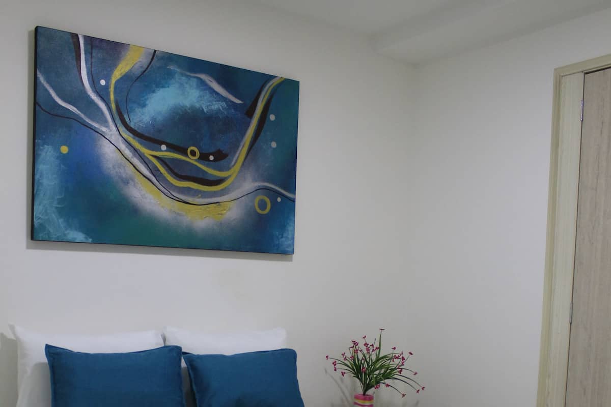 A neatly made bed with blue and white bedding, a blue throw blanket, and a small potted plant on a bedside table.