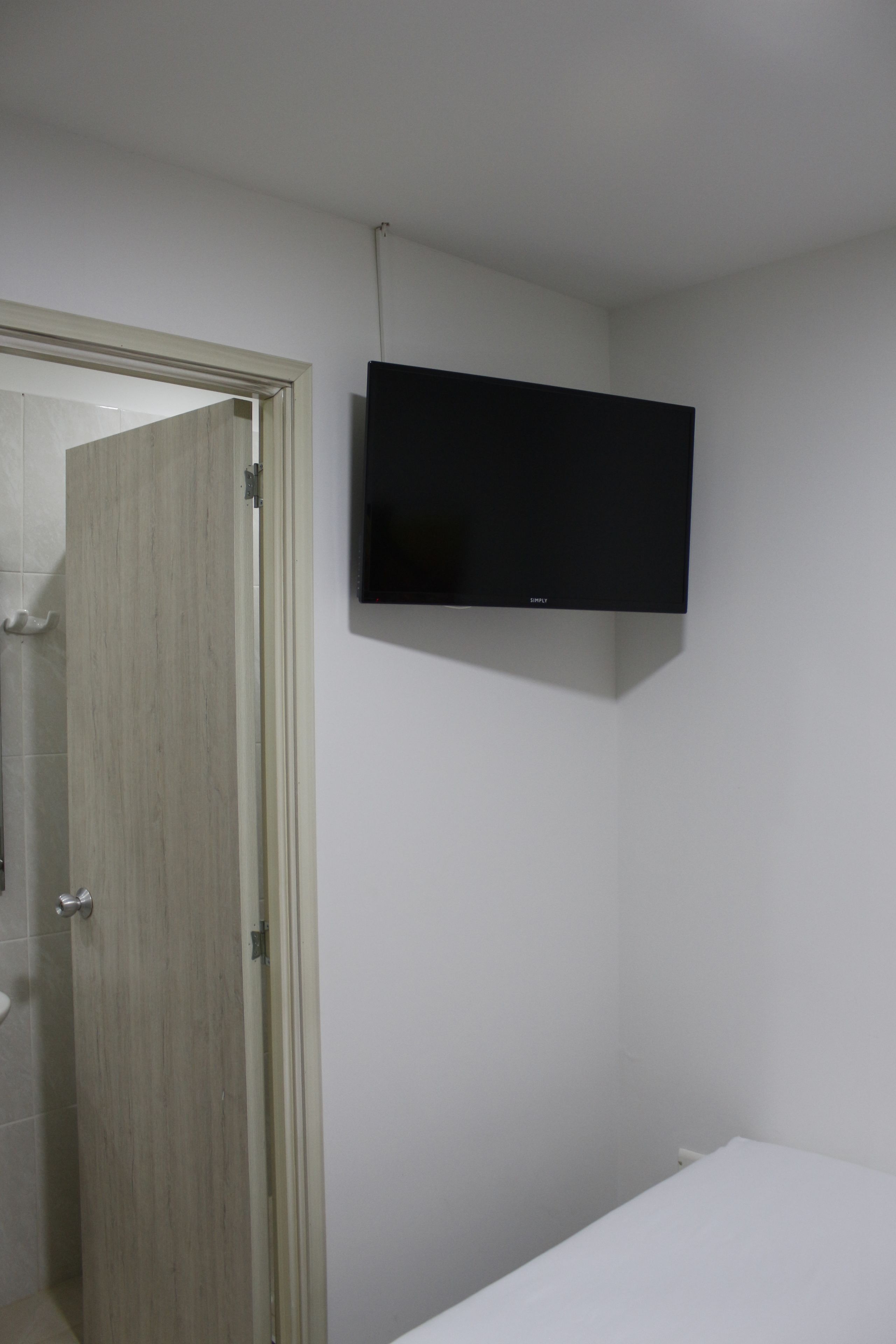 Une salle de bain avec une porte en bois, un lavabo blanc et un téléviseur fixé au mur.
