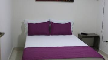 A bedroom with a bed, a nightstand, a wall-mounted fan, and a painting.