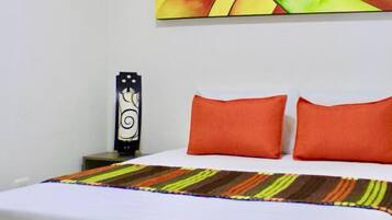 Habitación de hotel con una cama, dos almohadas naranjas, una manta colorida a rayas, una obra de arte colgada en la pared y un objeto decorativo en la mesita de noche.