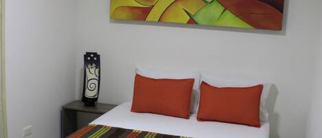 A hotel room with a bed, a nightstand, a wall-mounted fan, and a painting.