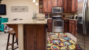 A kitchen with wooden cabinets, a stainless steel refrigerator, a microwave, an oven, and a bar area with stools. - Happy Cow RG108 2 Bedroom Condo by RedAwning (New Braunfels)
