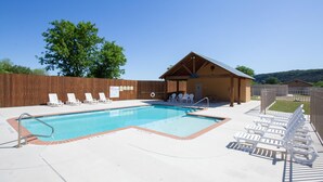 A rectangular swimming pool with a wooden deck, surrounded by white lounge chairs and a covered seating area. - Happy Cow RG108 2 Bedroom Condo by RedAwning (New Braunfels)
