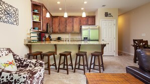 A modern kitchen with wooden cabinets, a stainless steel refrigerator, and a bar area with stools. - Happy Cow RG108 2 Bedroom Condo by RedAwning (New Braunfels)