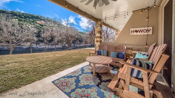 An outdoor patio with wooden chairs and a table, a decorative rug, and a sign that reads "HOWDY". - Happy Cow RG108 2 Bedroom Condo by RedAwning (New Braunfels)