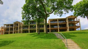 A multi-story hotel with a staircase leading to the entrance, surrounded by well-maintained grass and trees. - Happy Cow RG108 2 Bedroom Condo by RedAwning (New Braunfels)