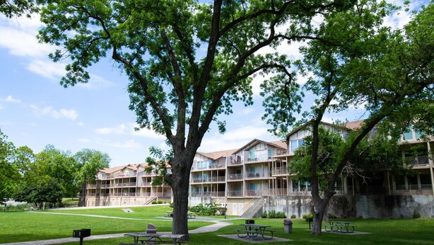 Un hotel de varios pisos con balcones, un patio con césped y mesas de picnic.