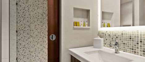Un baño moderno con un espejo grande, un lavabo blanco y una zona de ducha con mosaicos.