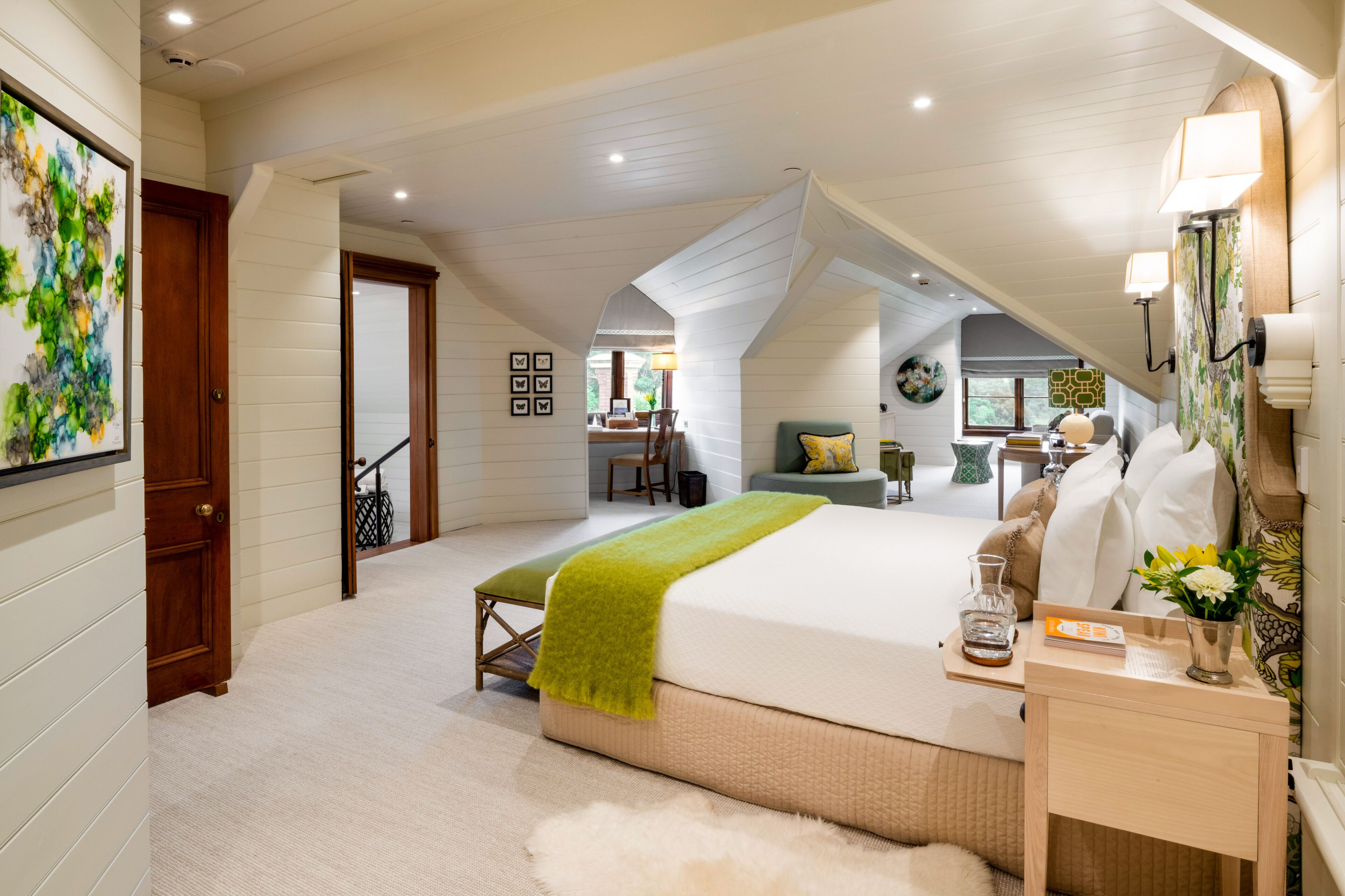 A bedroom with a large bed, a bedside table, a lamp, and a view of the dining area.