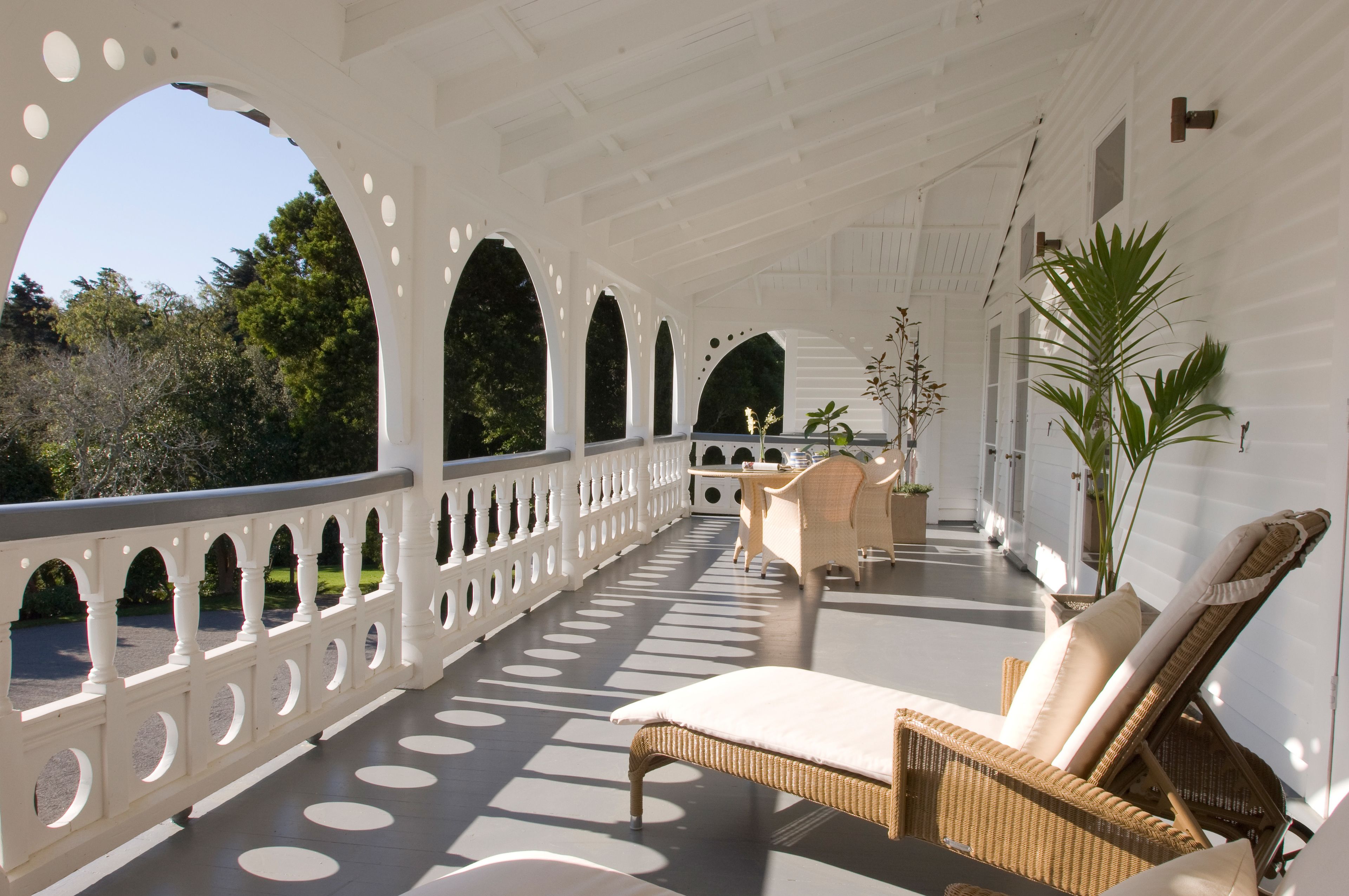 A covered outdoor area with wicker furniture, white railings, and potted plants.