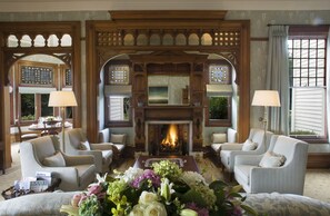 A cozy living room with a fireplace, comfortable seating, and a floral arrangement. - Otahuna Lodge (Tai Tapu)