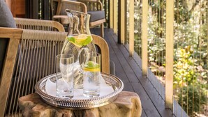 Una terraza de madera con una mesa que sostiene una jarrón, vasos y una bandeja.