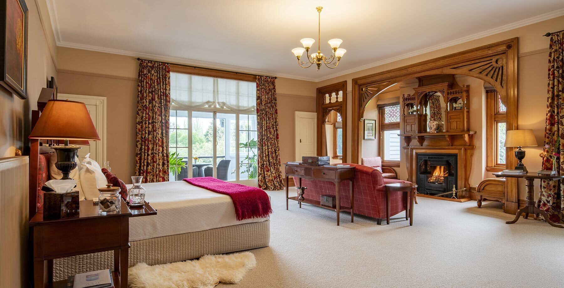 A spacious hotel room with a large bed, a desk, a fireplace, and a view of the outdoors.