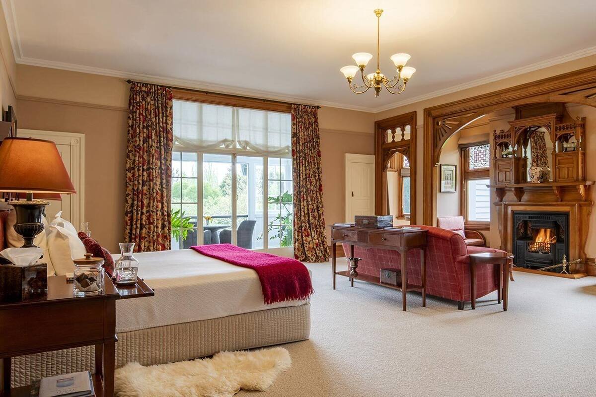 A spacious hotel room with a large bed, a desk, a fireplace, and a view of the outdoors.