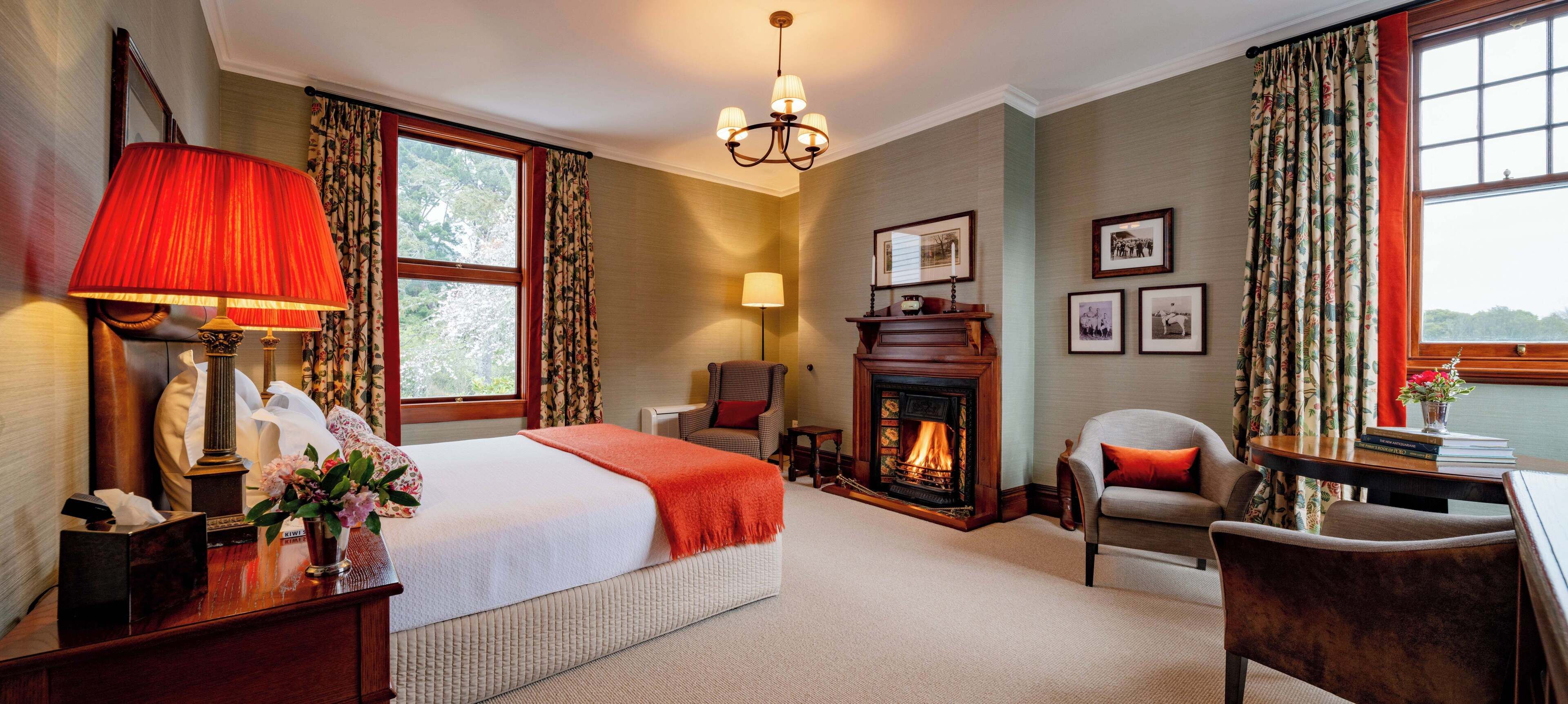 A hotel room with a bed, a fireplace, a desk, a chair, and a window with curtains.