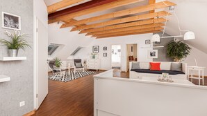 Un loft moderno con vigas de madera a la vista, una cama en altillo, una zona de comedor y una cocina.