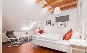 A bedroom with a sloped ceiling, a skylight, a bed, a desk, a chair, and a radiator.
