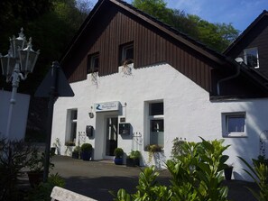 Un bâtiment blanc avec un toit brun, une enseigne indiquant « Entrée de l’hôtel Rutherbach  », et des plantes en pot devant l’entrée.
