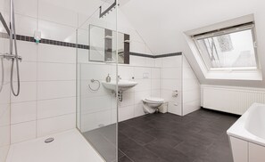 Une salle de bain moderne dotée d’une douche à parois de verre, d’un lavabo blanc, de toilettes et d’une fenêtre laissant entrer la lumière naturelle.