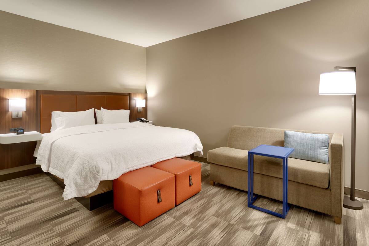 A hotel room with a bed, a sofa, a small table, and a lamp.