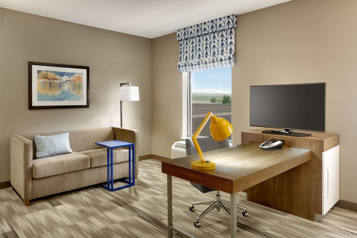 A hotel room with a sofa, desk, TV, lamp, and a painting.