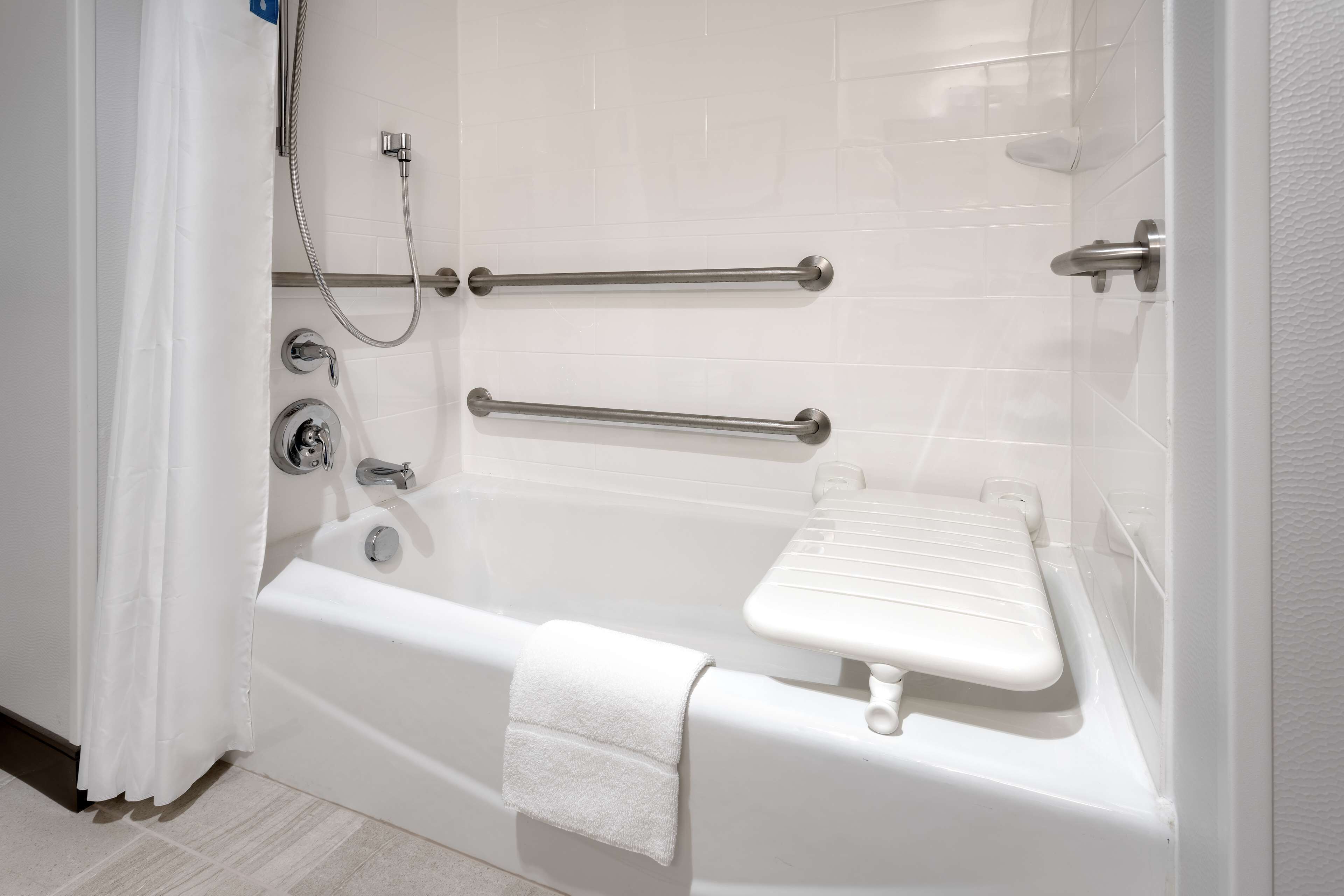 Una bañera blanca con barras de apoyo, una toalla y un cabezal de ducha manual.