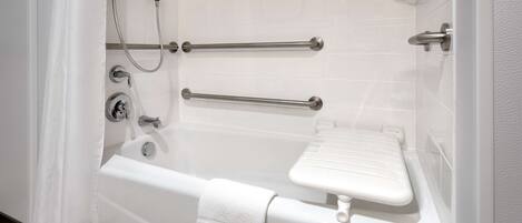 Una bañera blanca con barras de apoyo, una toalla y un cabezal de ducha manual.