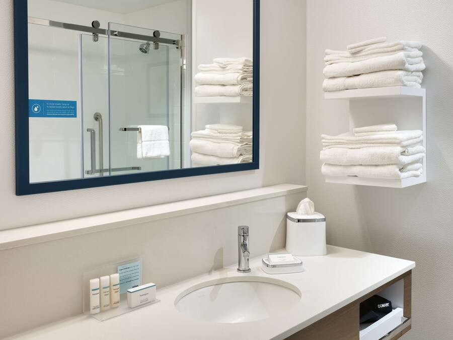 A modern bathroom with a large mirror, a sink, and neatly stacked towels on shelves.