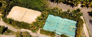 Une vue aérienne d’un court de tennis entouré d’une végétation luxuriante et de palmiers.