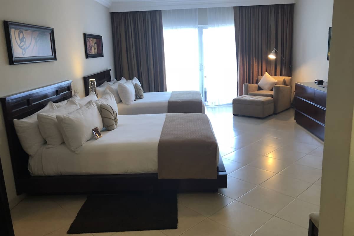 Habitación de hotel con dos camas, un sofá, un escritorio y un ventanal con cortinas.