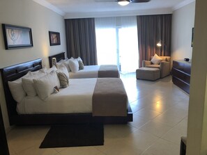 Habitación de hotel con dos camas, un sofá, un escritorio y un ventanal con cortinas.