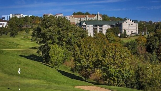 A golf course with a flagstick, surrounded by lush greenery and residential buildings in the background. - Green Mountain Grand 4 Bedroom Condo by RedAwning (Branson)