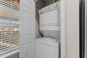 A compact laundry area with a front-loading washer and dryer, a door, and a window with blinds. - Green Mountain Grand 4 Bedroom Condo by RedAwning (Branson)