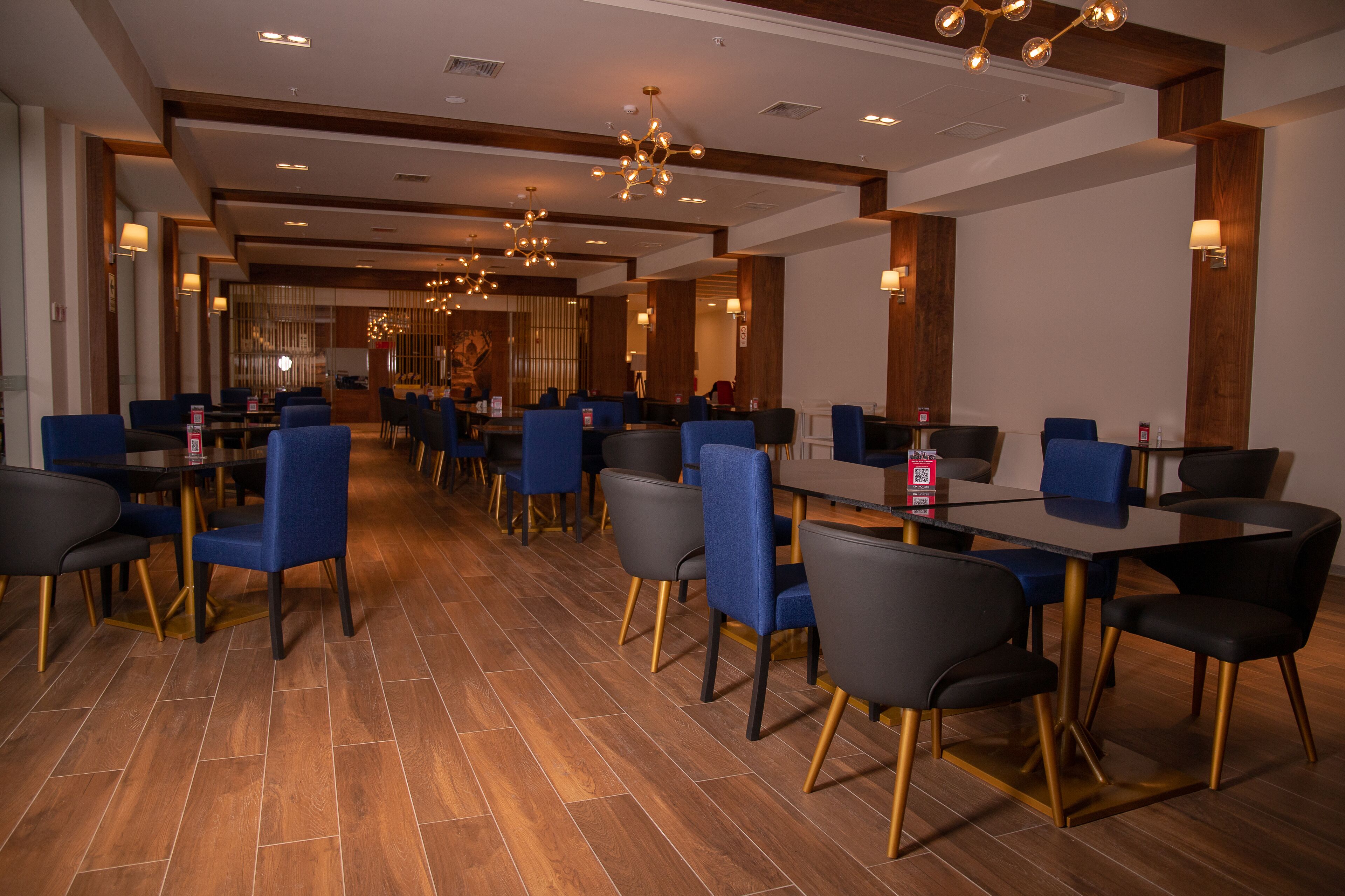 Um restaurante espaçoso com várias mesas e cadeiras, piso de madeira e luminárias modernas.