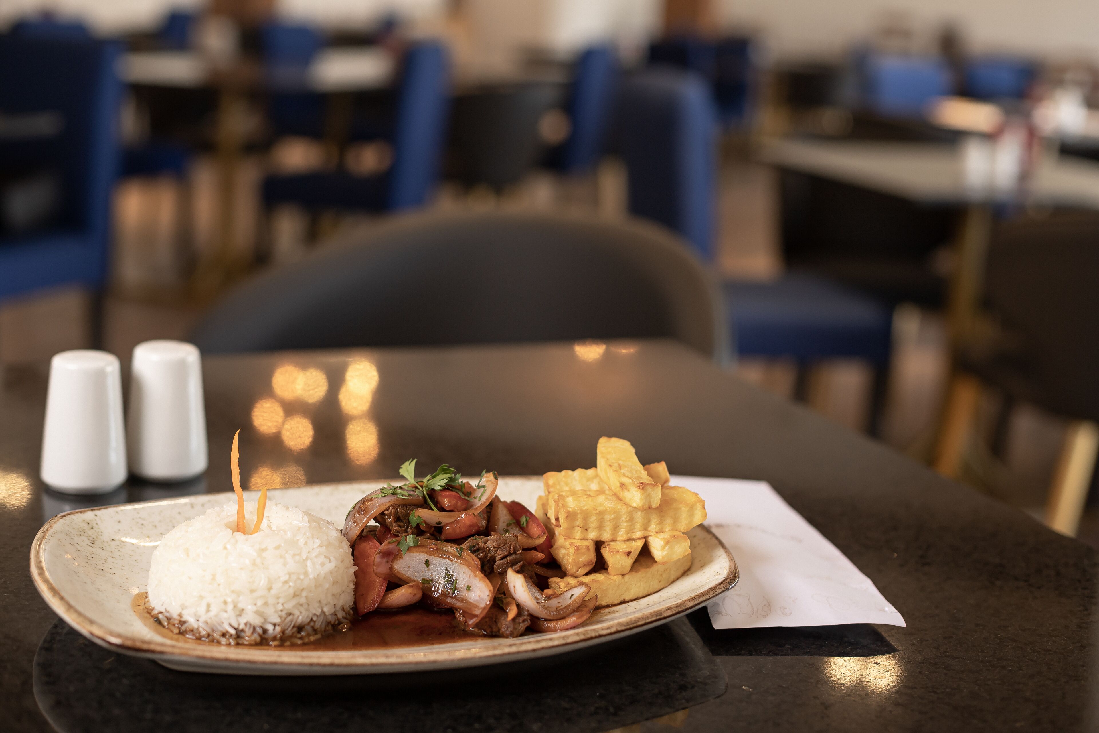 A plate of food with rice, meat, and plantains on a table in a restaurant.