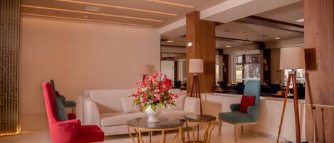 A modern living room with a white sofa, red and teal chairs, and a coffee table with a vase of flowers.