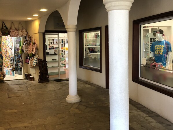 A corridor with a shop on the left displaying bags and a mannequin in the window on the right.