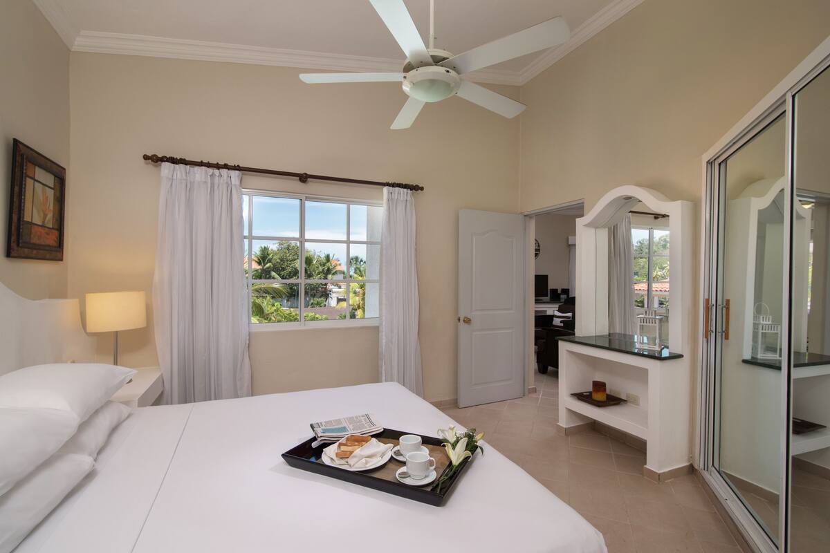 Une chambre d’hôtel avec un lit, un plateau contenant des articles pour le petit-déjeuner, un ventilateur de plafond et une vue sur l’extérieur.